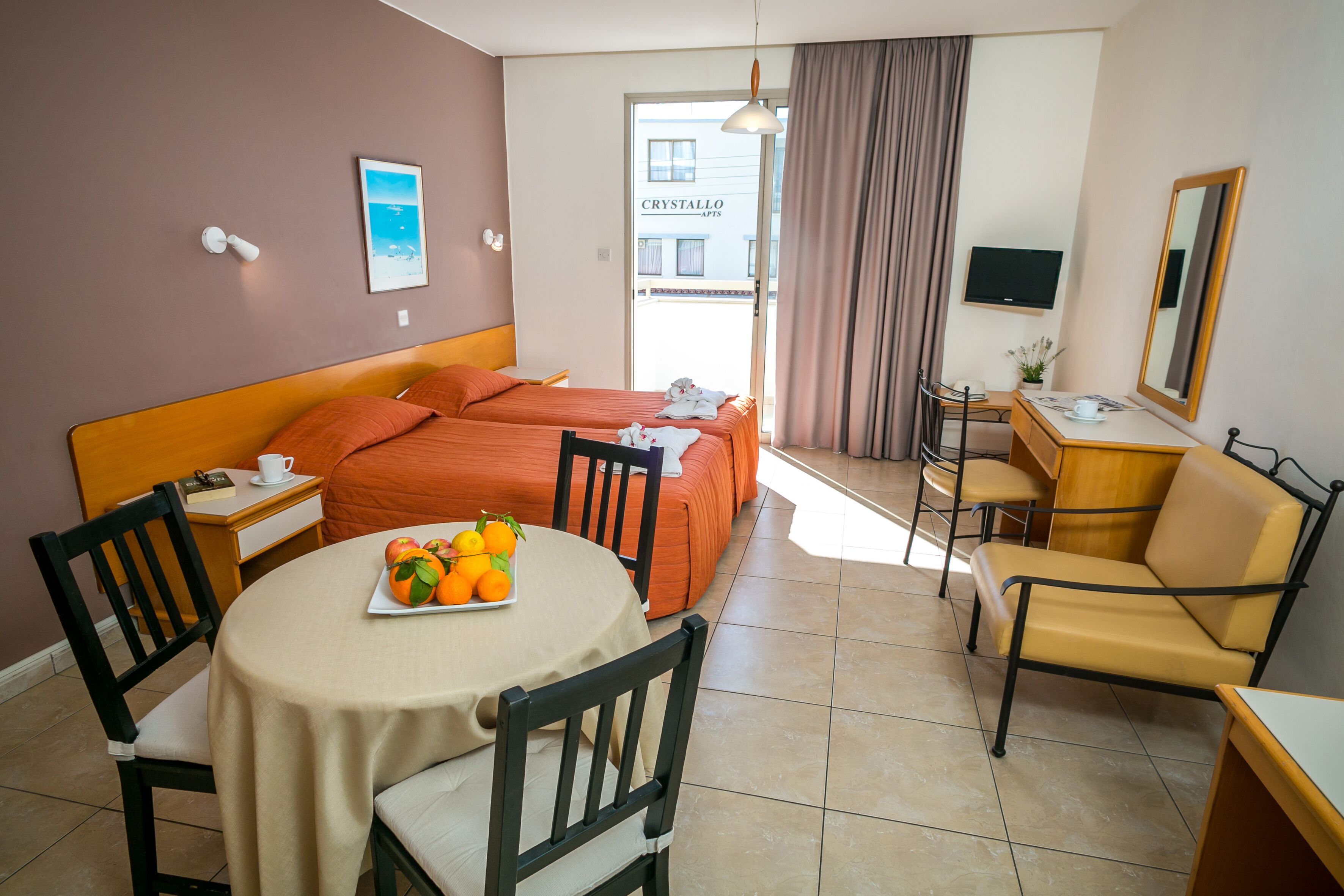 Une chambre d’hôtel avec un lit, un bureau, une chaise, une table avec des fruits et un téléviseur.