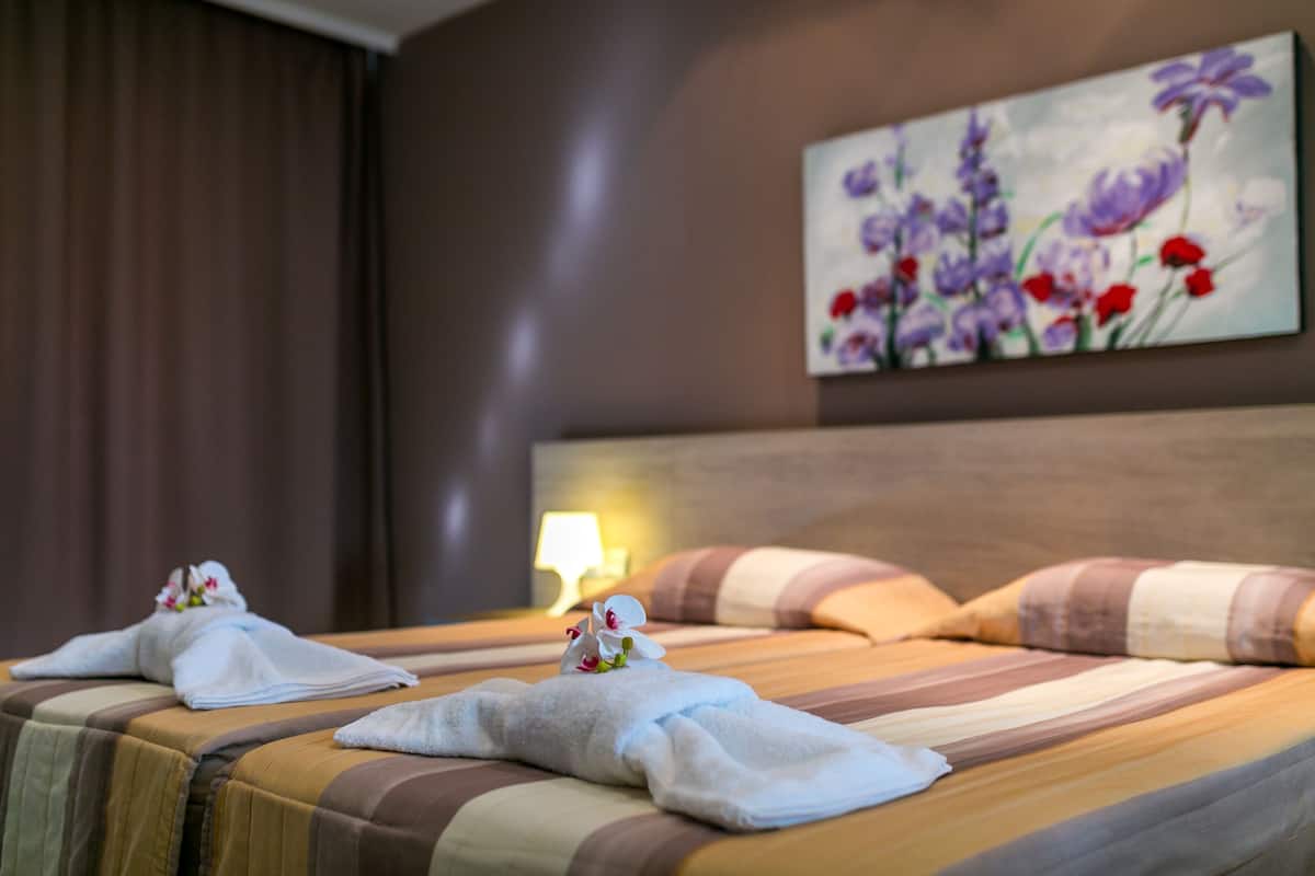 Habitación de hotel con dos camas, ropa de cama a rayas, un cuadro de flores en la pared y una lámpara en la mesita de noche.