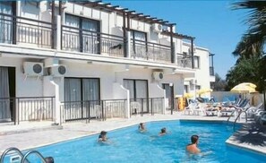 A hotel with a swimming pool, multiple balconies, and sun loungers. - Crystallo Apartments (Paphos)