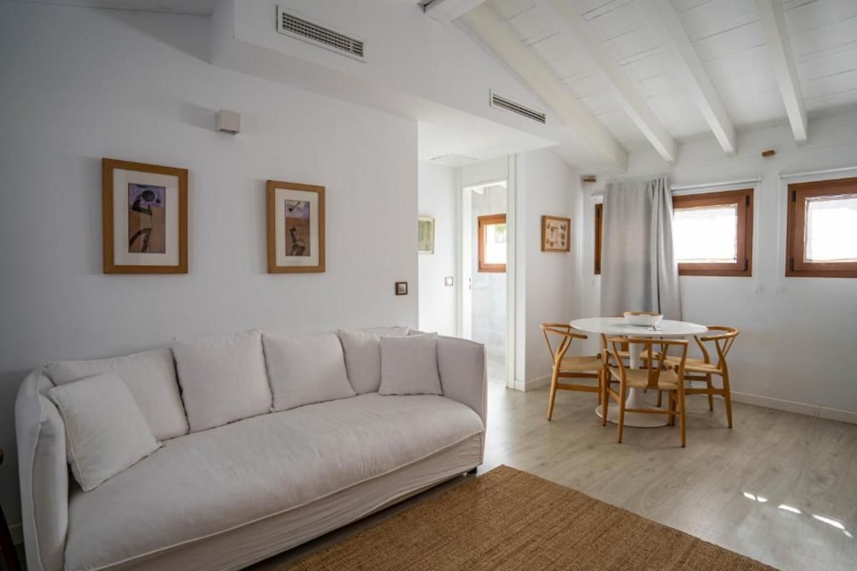A modern living room with a sofa, a dining table with chairs, and framed pictures on the walls.