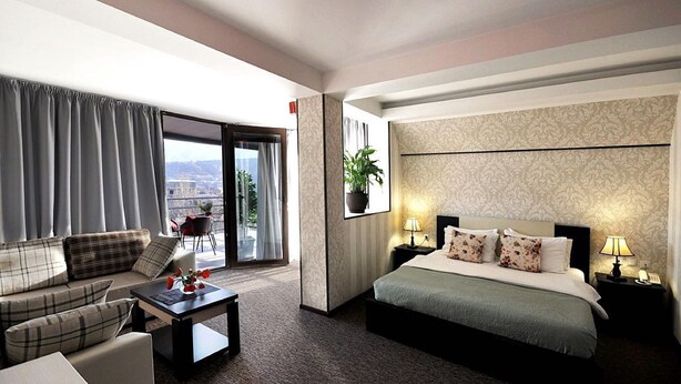 A hotel room with a sofa, a bed, a desk, and a view of the city through the window. - Light House - Old City (Tbilisi)