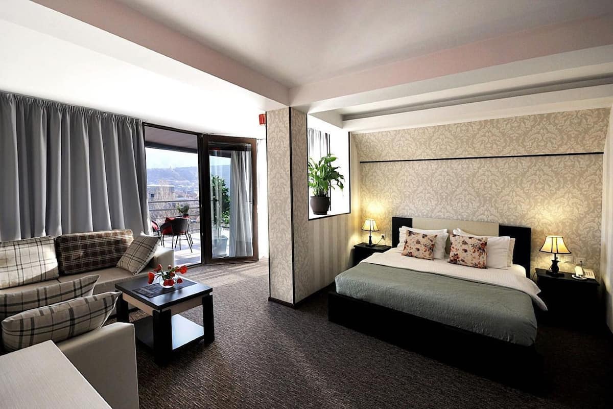 A hotel room with a sofa, a bed, a desk, and a view of the city through the window.