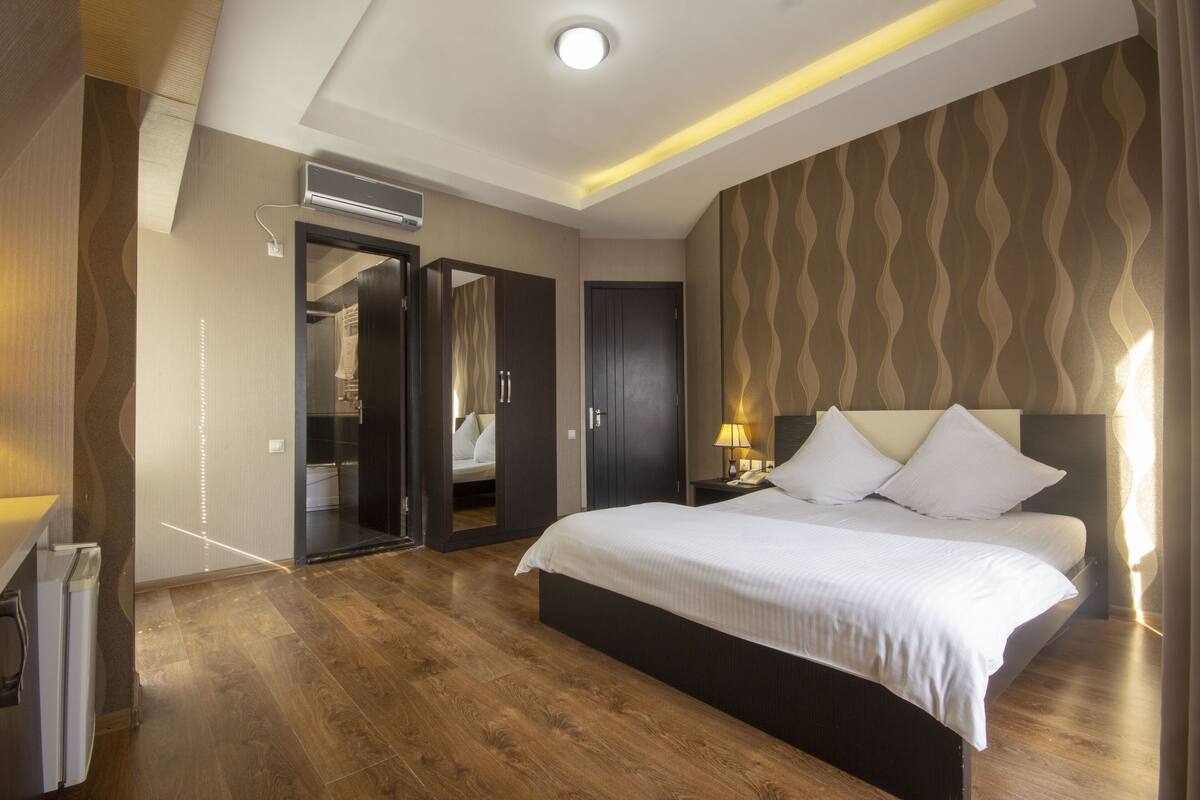 A modern hotel room with a large bed, a walk-in closet, and a bathroom with a glass partition.