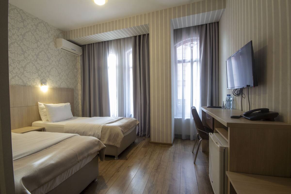 A hotel room with two beds, a desk with a telephone, a television, and an air conditioning unit.