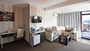 A hotel room with a TV, a desk, a sofa, a coffee table, and a view of the city. - Light House - Old City (Tbilisi)