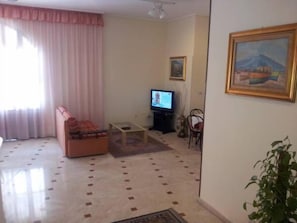 Ein Wohnzimmer mit einer Couch, einem Fernseher und einem Bild an der Wand.