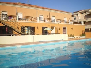 Ein Pool neben einem Gebäude mit einem Ziegeldach, einer Treppe und einem kleinen überdachten Bereich mit einem Sonnenschirm.