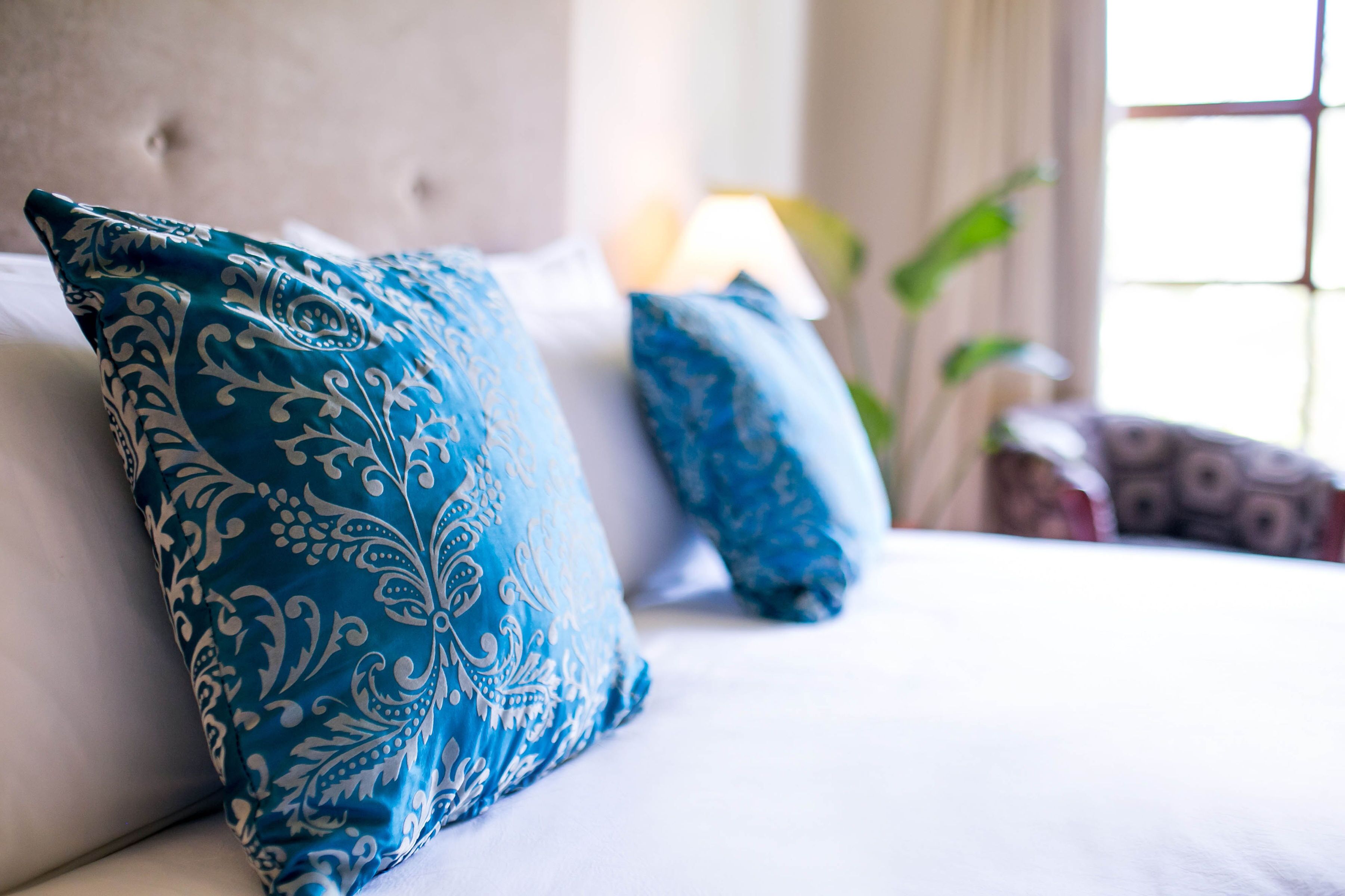 Een bed met blauwe, geborduurde kussens en een gestuufd hoofdbord.