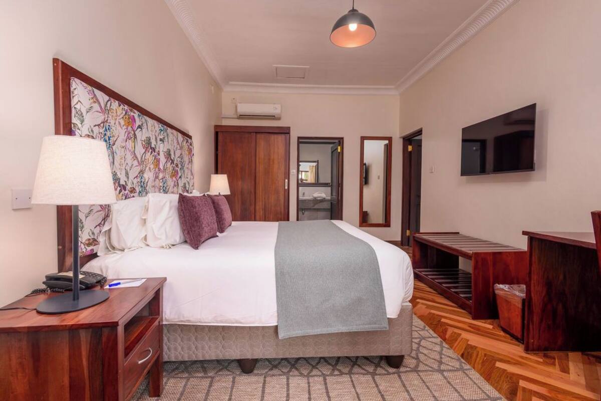 A hotel room with a large bed, two bedside tables, a desk, a chair, a TV, and a wardrobe.