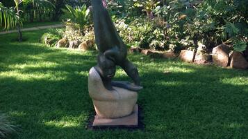 A sculpture of a person in a dynamic pose on a pedestal in a garden with grass, rocks, and various plants.