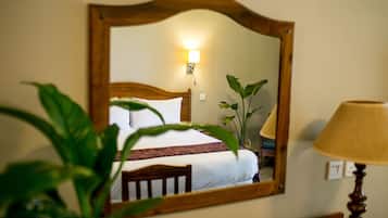 A neatly made bed with a wooden headboard, a bedside lamp, and a wall-mounted mirror reflecting the room.