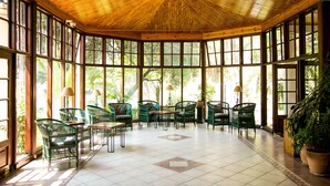 A spacious room with large windows, green wicker chairs, and a tiled floor.