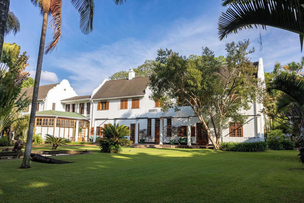 Un grand bâtiment de style colonial, peint en blanc, avec un toit végétalisé, entouré d’une végétation luxuriante et de palmiers.