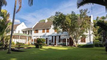 Un gran edificio de estilo colonial blanco con techo verde, rodeado de abundante vegetación y palmeras.