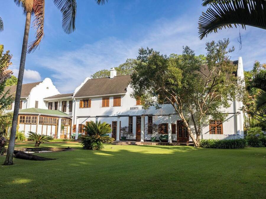 Un gran edificio de estilo colonial blanco con techo verde, rodeado de abundante vegetación y palmeras.