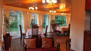 A dining area with wooden tables and chairs, a red sofa, and a chandelier.