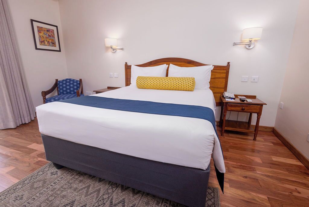 Una habitación de hotel con una cama grande, dos mesitas de noche, una silla y una lámpara de pared.