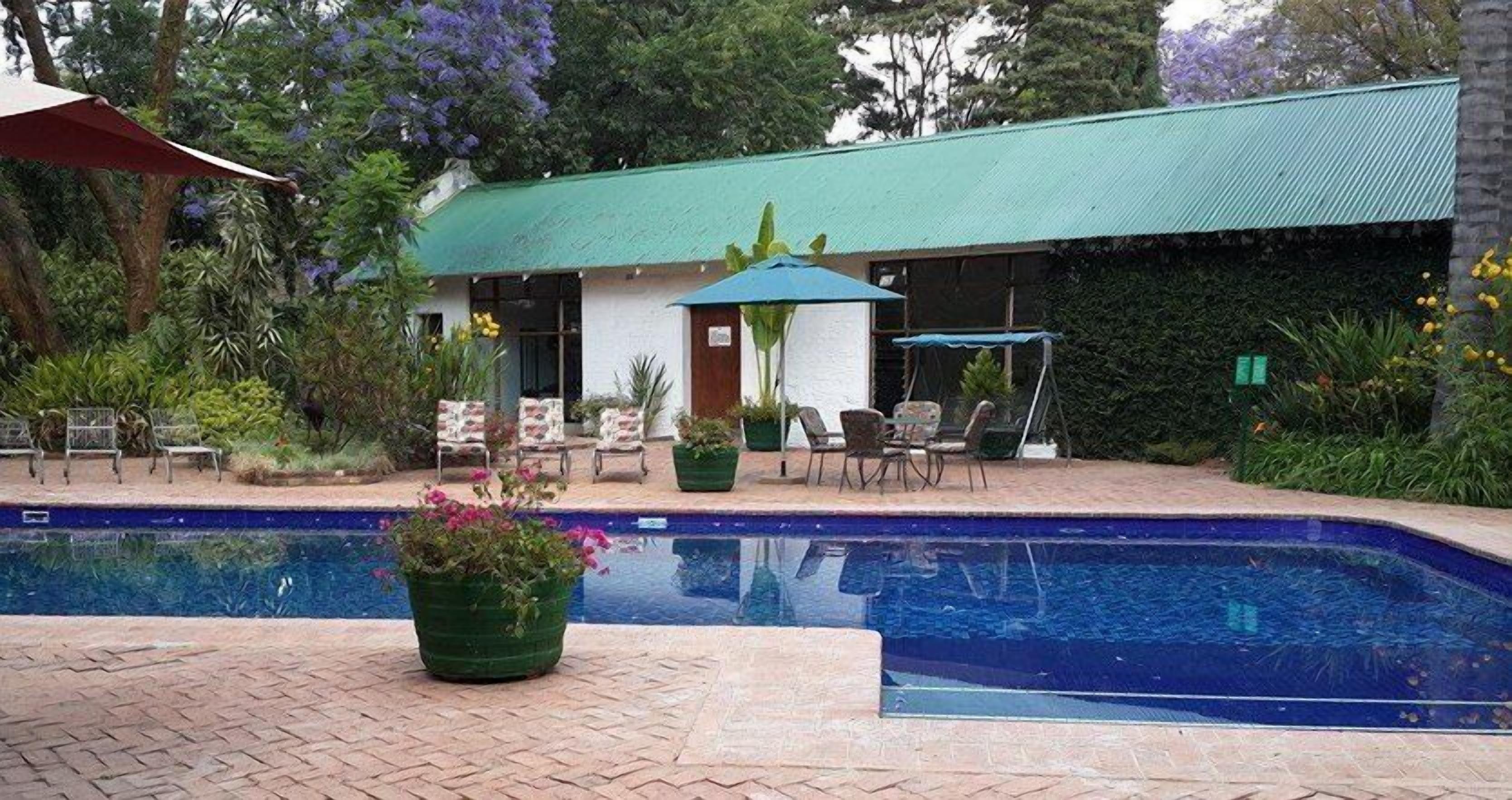 A pool area with a green-roofed building, outdoor seating, and potted plants.