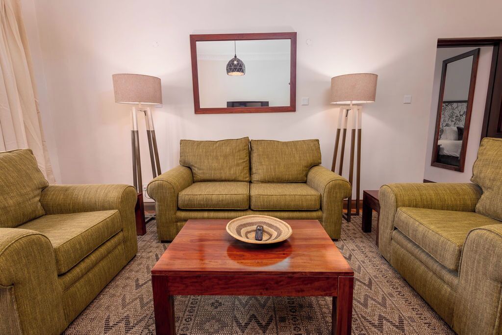 A living room with a sofa set, two floor lamps, a mirror, and a patterned rug.