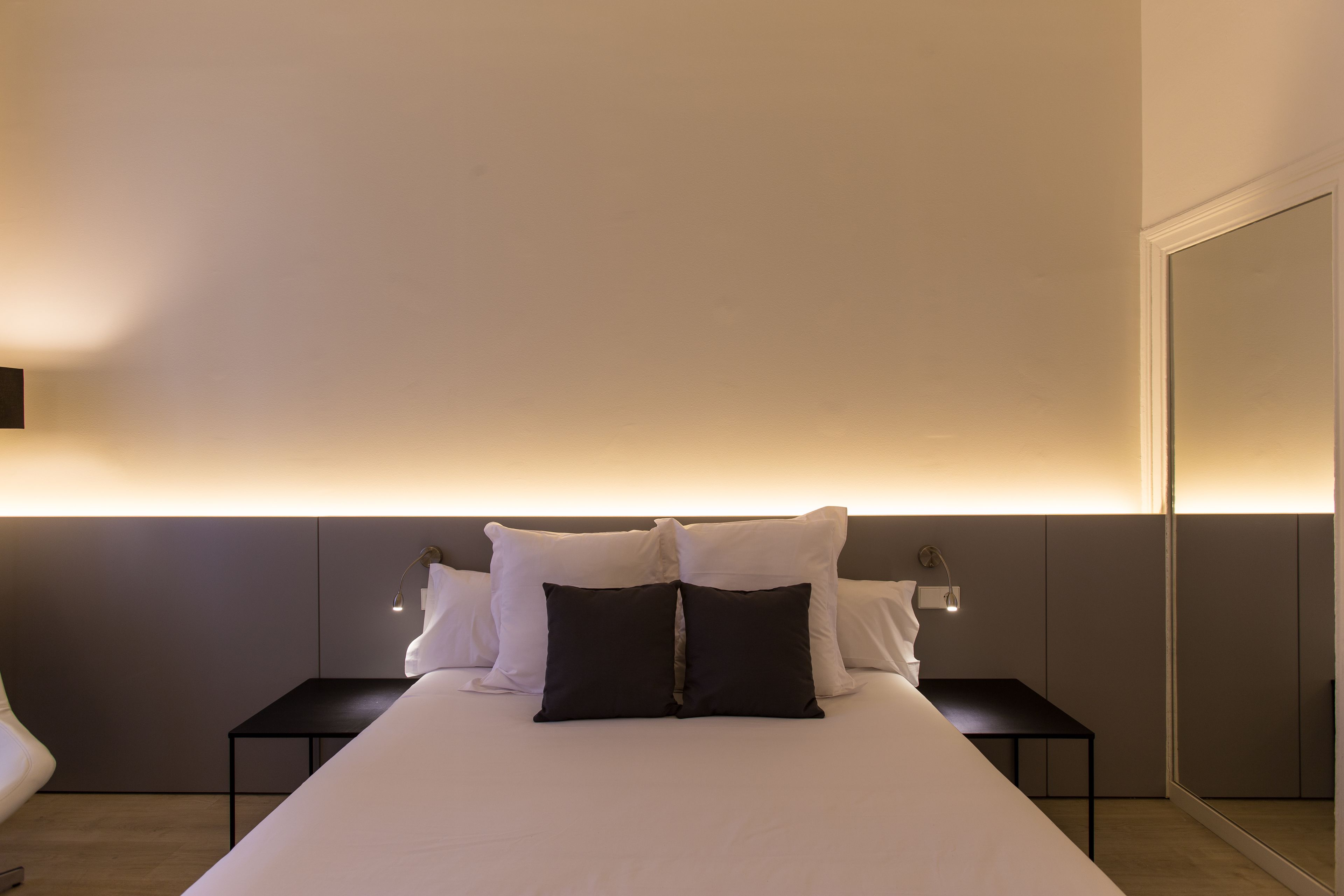 Ein modernes Hotelzimmer mit einem großen Bett, zwei Nachttischen, einer Ablagefläche und einer Wandlampe.