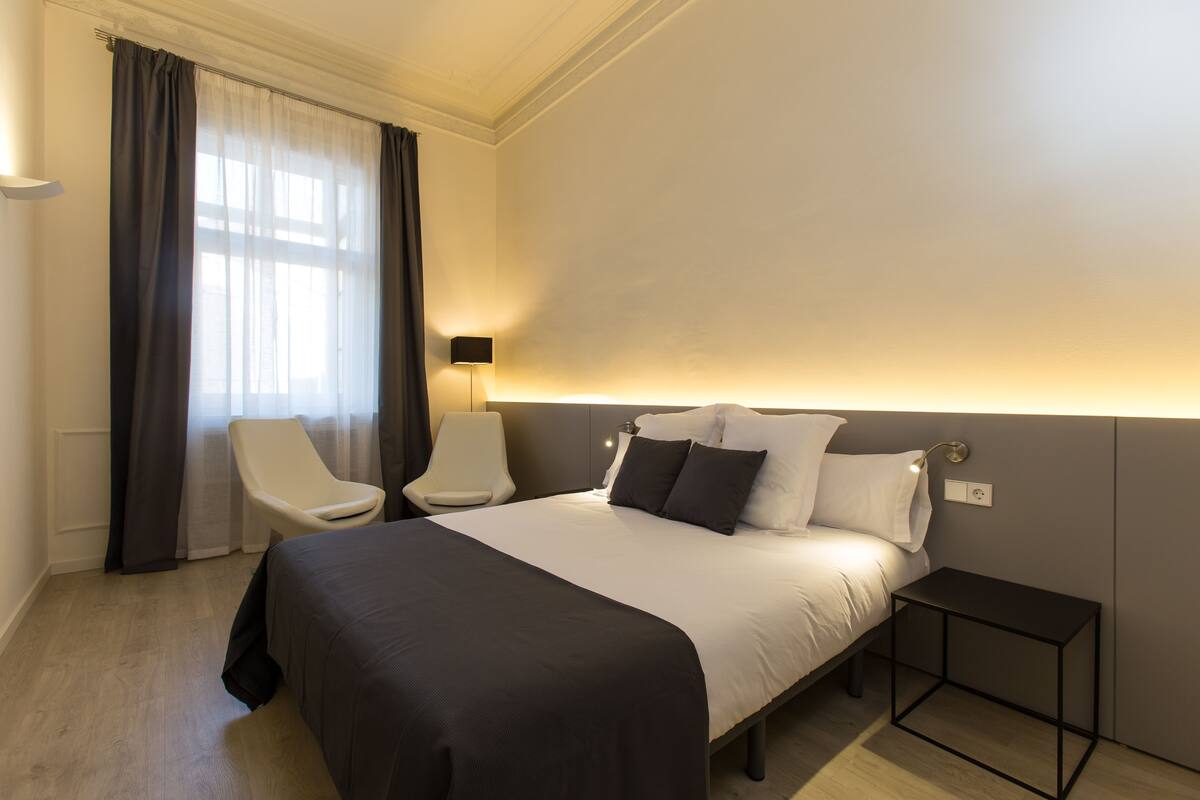 Een hotelkamer met een groot bed, nachtkastje, een stoel en een lamp.