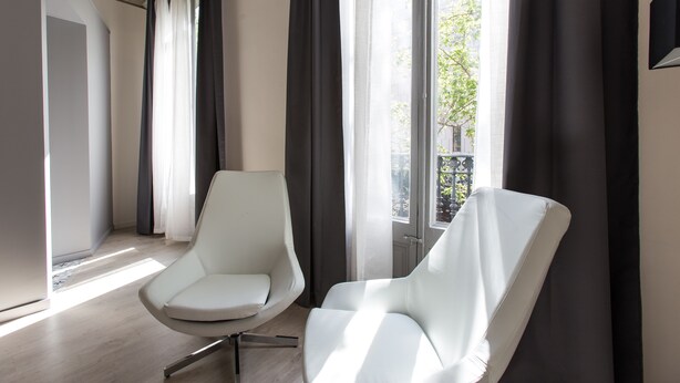 Una sala de estar moderna con dos sillones blancos, ventanas amplias con cortinas y vista a un árbol.