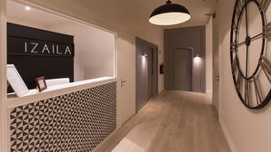 Un área de recepción con un muro de diseño geométrico, un reloj grande y un letrero que dice "IZAILA".