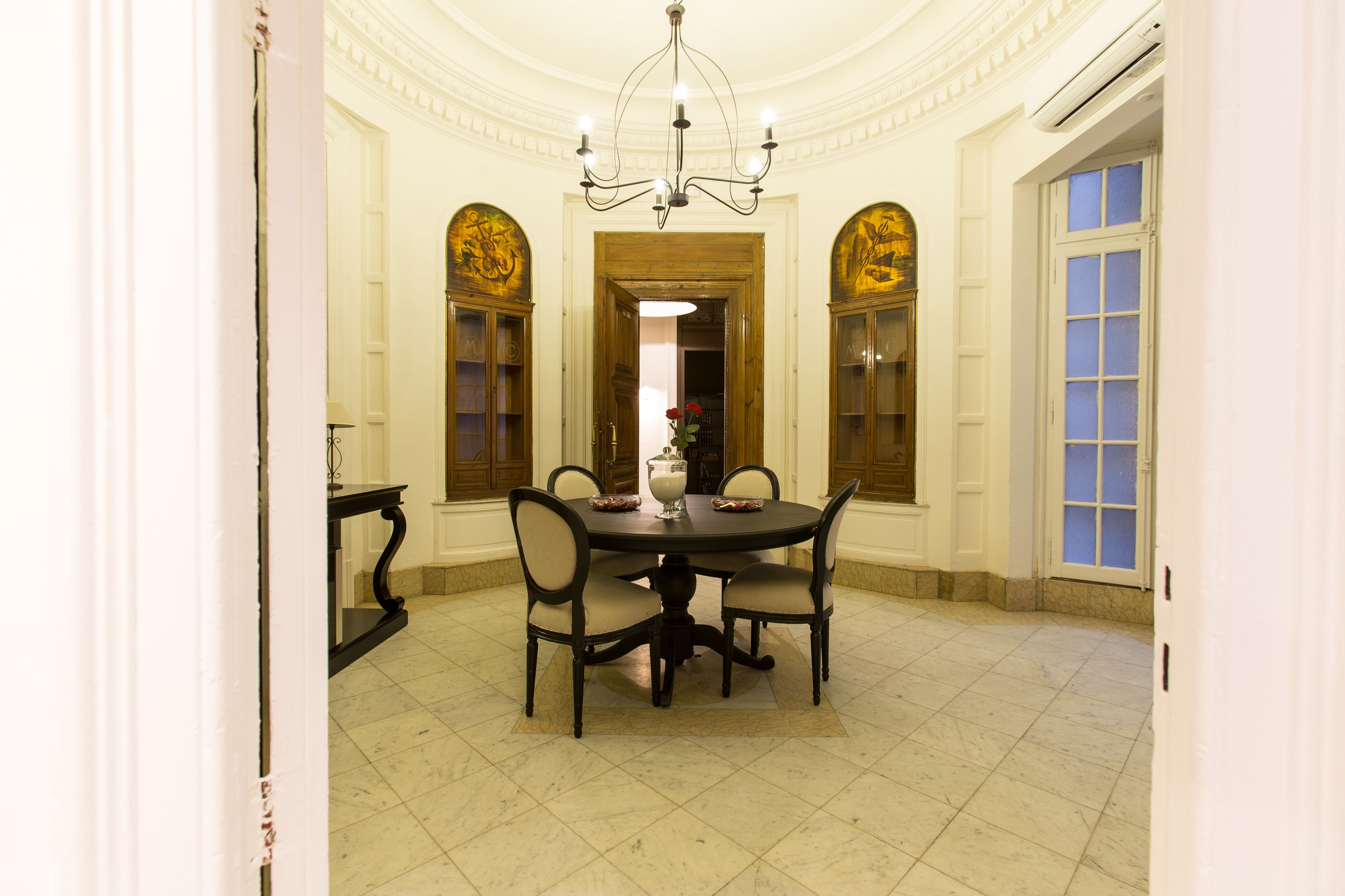 Un comedor elegante con una mesa redonda, cuatro sillas, una araña y paneles decorativos en las paredes.