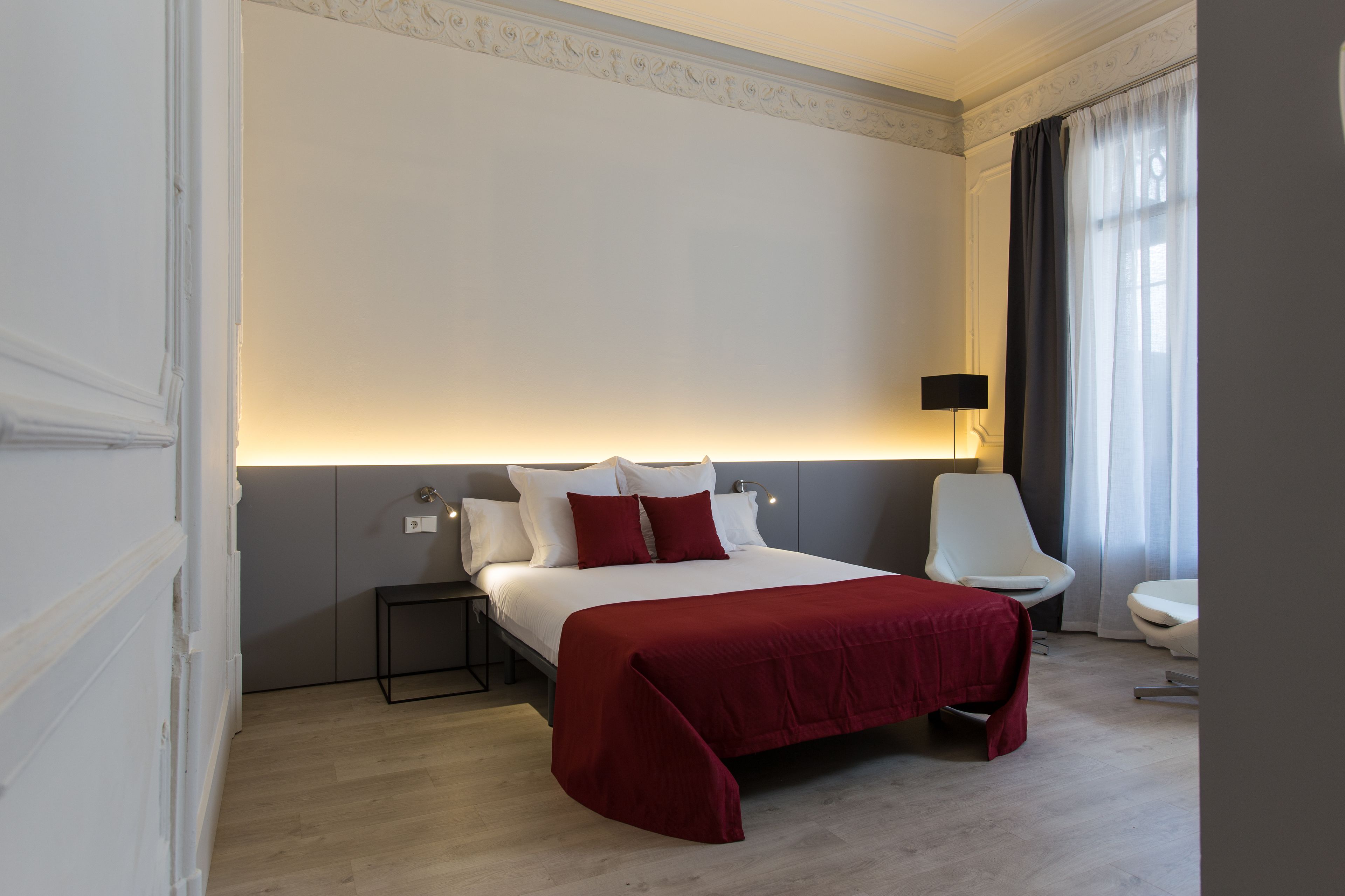 Una habitación de hotel con una cama grande, una mesita de noche, una silla y una lámpara.