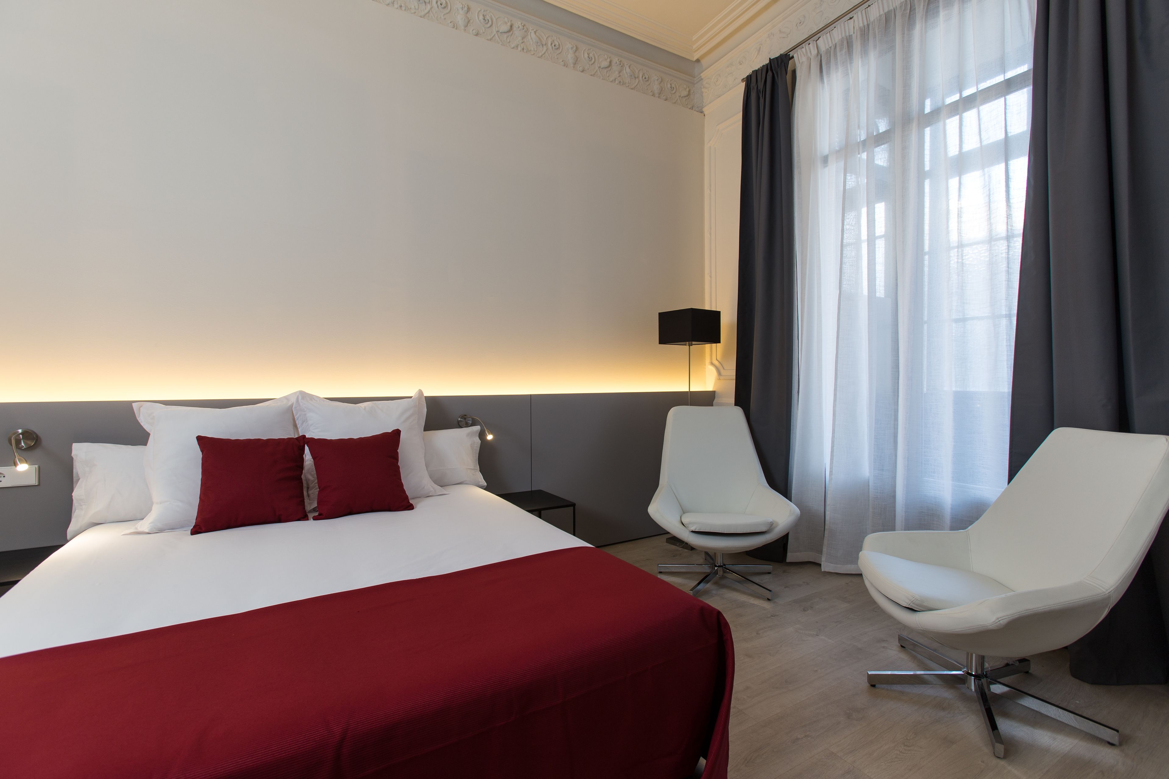 Una habitación de hotel con una cama grande, un sillón blanco, una mesita auxiliar y una lámpara.