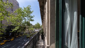 Un balcón estrecho con vistas a una calle de la ciudad, un edificio de arquitectura clásica y un cielo despejado.