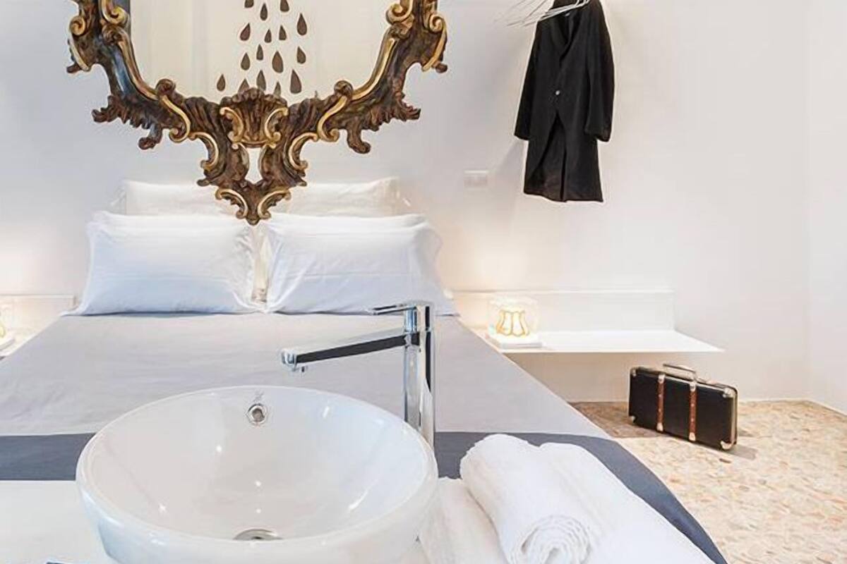 A modern hotel room with a large bed, a white sink, and a mirror with ornate detailing.