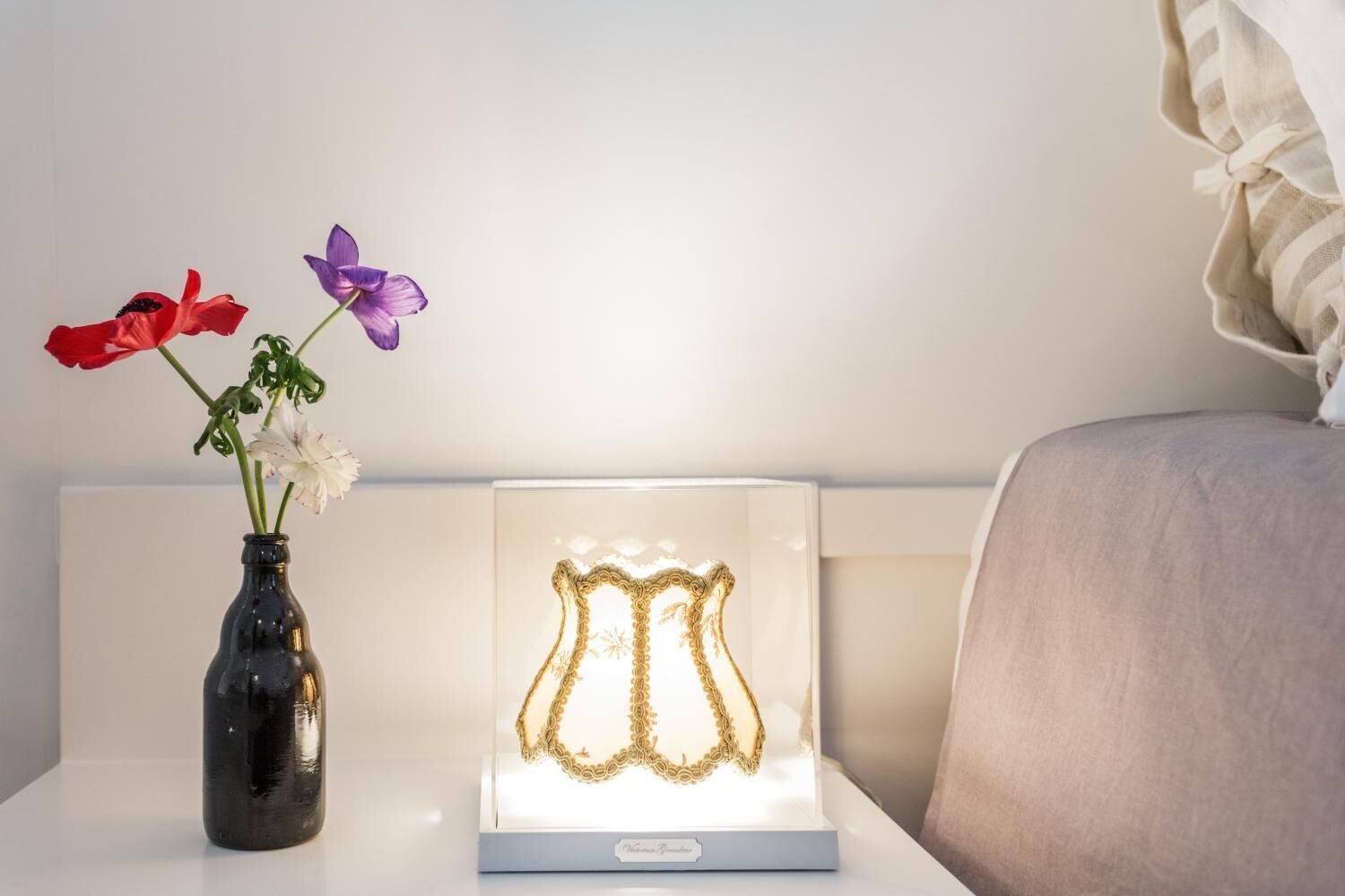 A bedside table with a vase of flowers and a decorative light.