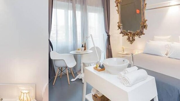 Una camera d'albergo moderna con un letto, un comodino con uno specchio, un piccolo tavolo rotondo con sedie e una finestra con tende.