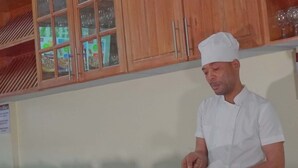 Een kok in een witte uniform kookt in een keuken met houten kastjes en een fornuis.