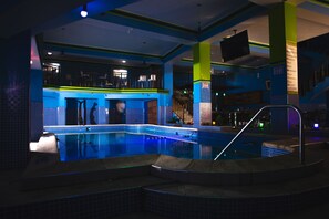 Une piscine à fond de verre, entourée de murs recouverts de carreaux bleus et dotée d’un balcon.