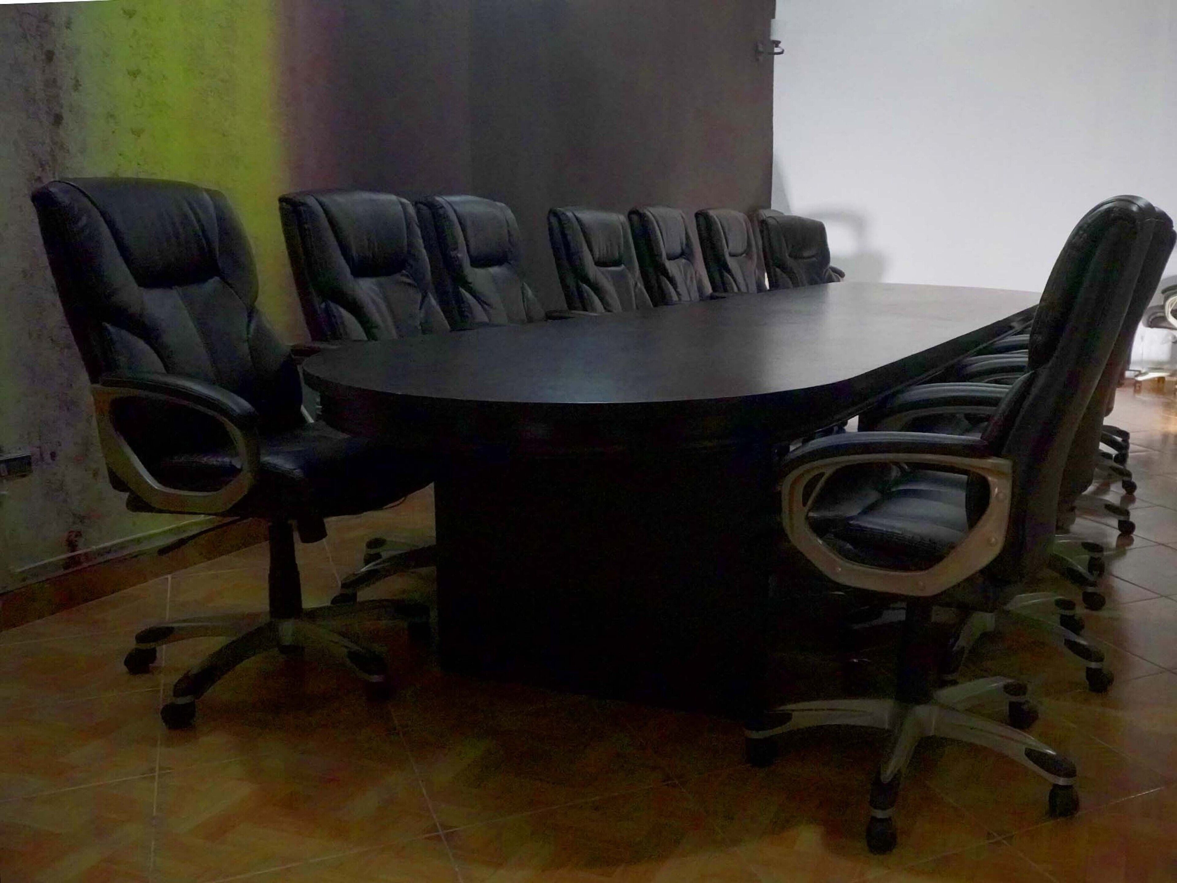 A conference room with a large round table and multiple black leather chairs.