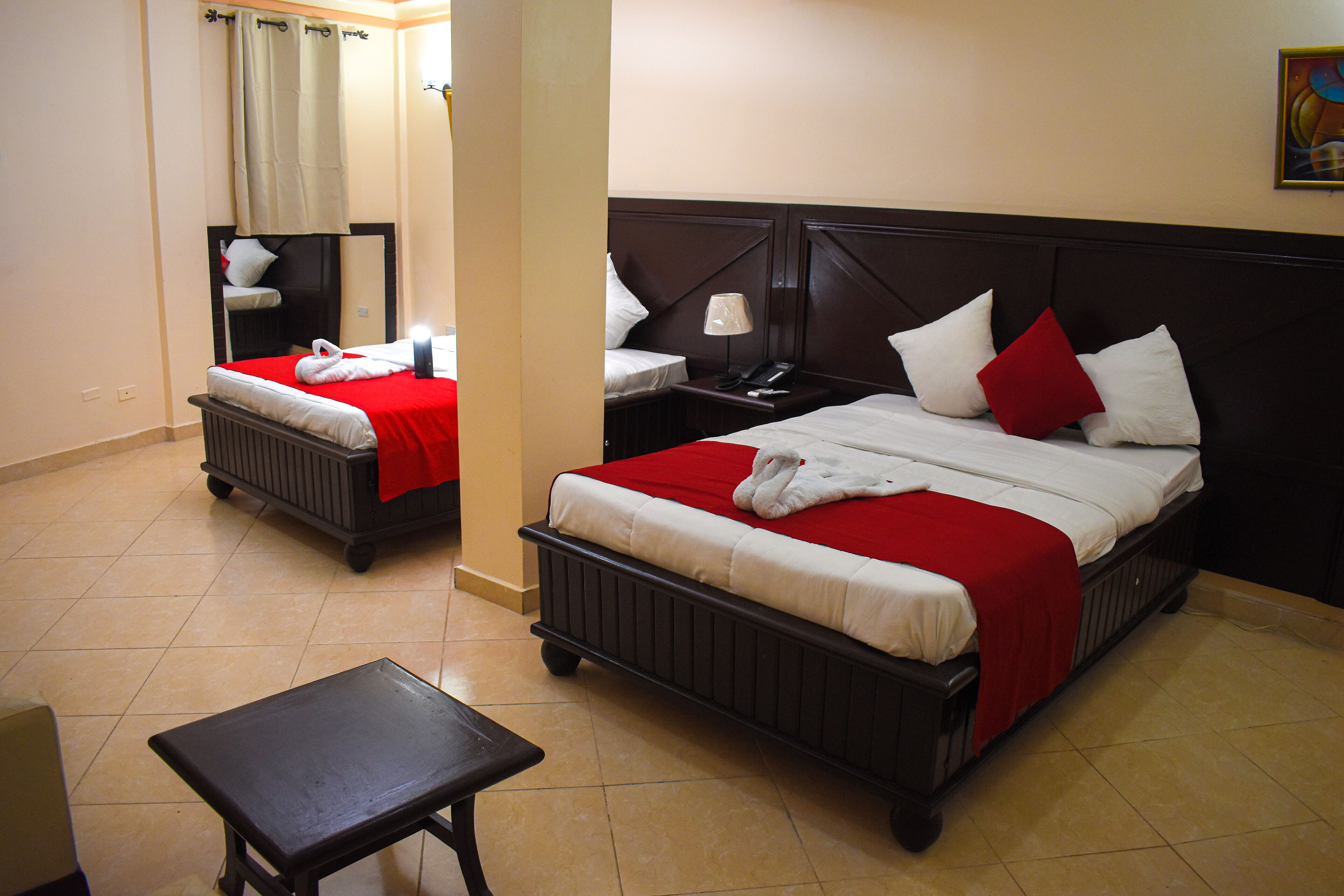 A hotel room with two beds, a nightstand, a table, and a mirror.