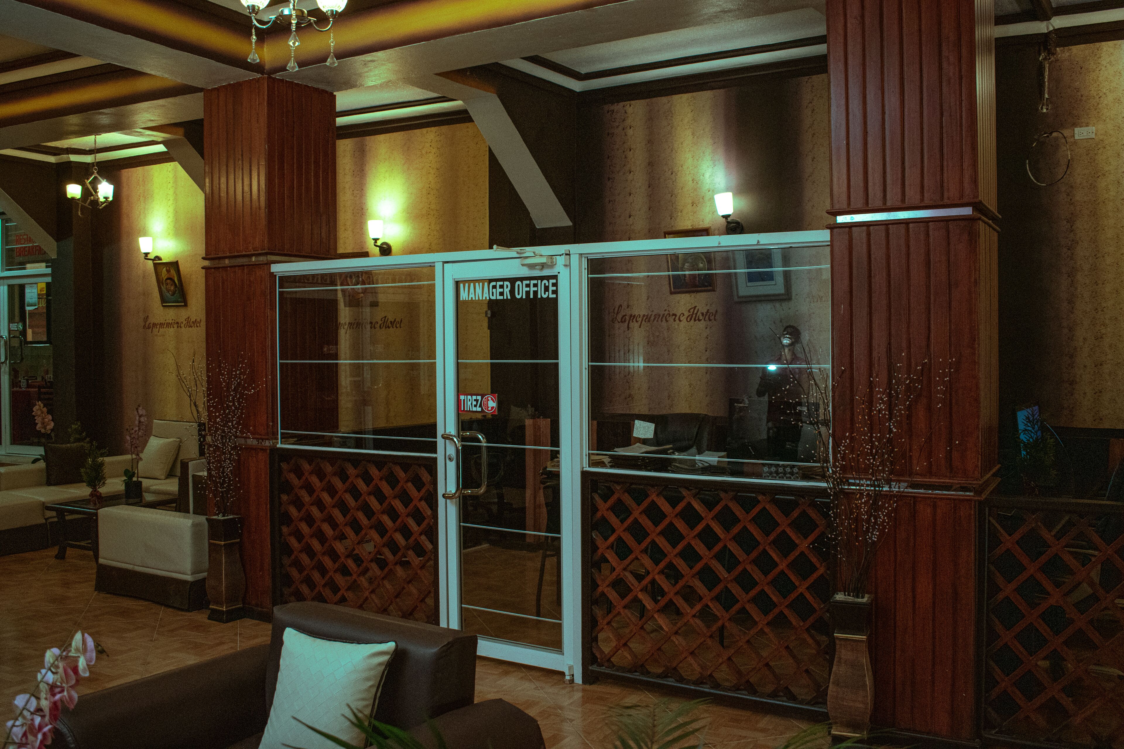 A manager's office with a glass door, wooden paneling, and a reception area with a sofa and decorative plants.