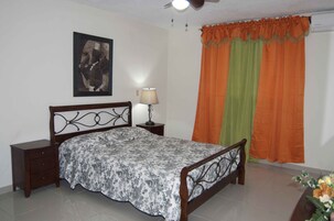 Un dormitorio con cama, mesita de noche, lámpara y un cuadro en la pared.