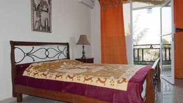 Un dormitorio con una cama de madera, una mesita de noche, una lámpara, un cuadro en la pared y un balcón con cortinas naranjas.