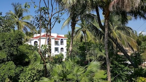A white building with a red roof surrounded by lush greenery and palm trees. - Hotel & Temazcal Hacienda de Melaque (San Patricio Melaque)