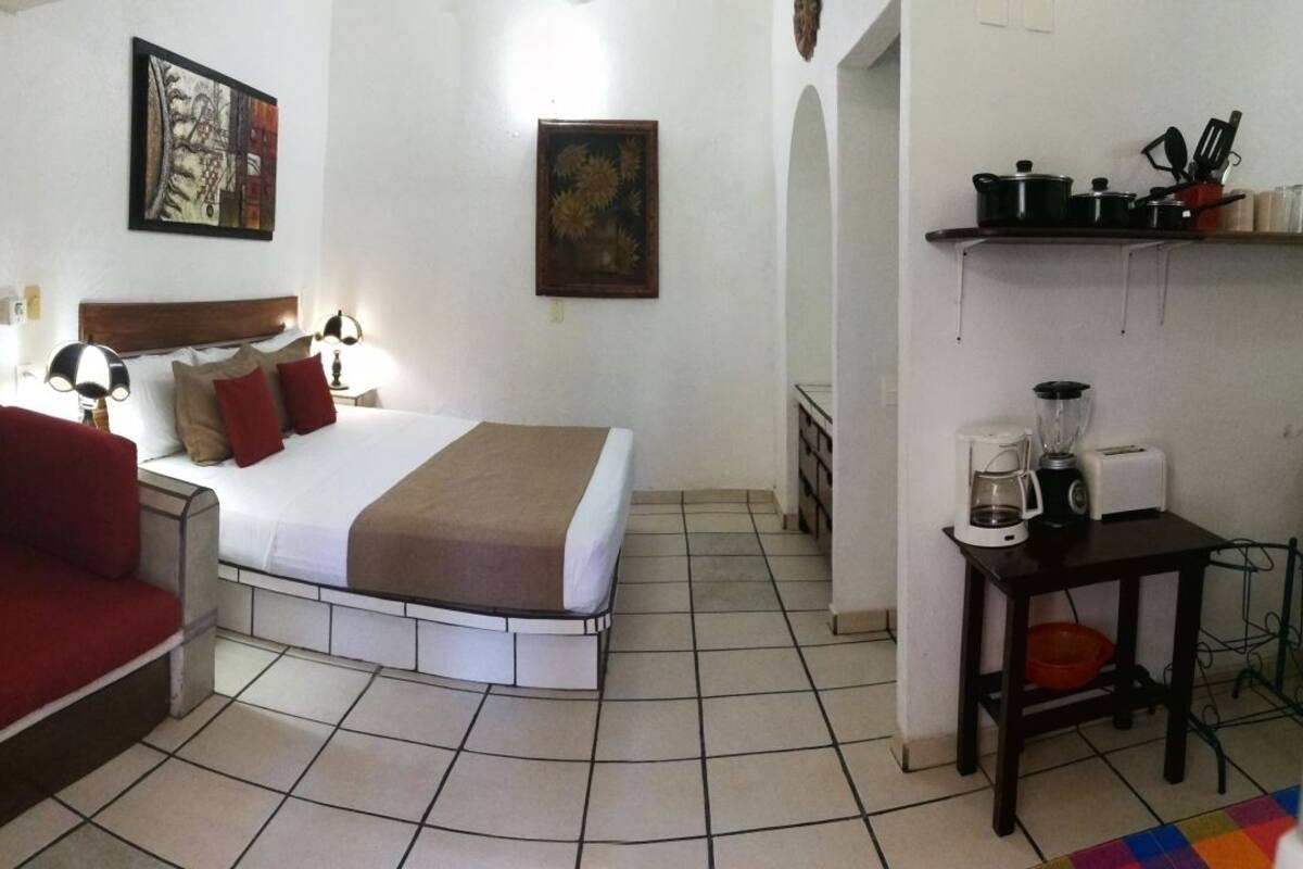 Une chambre à coucher avec un lit, un canapé rouge, une table de chevet avec une lampe et une petite table sur laquelle se trouve une machine à café.