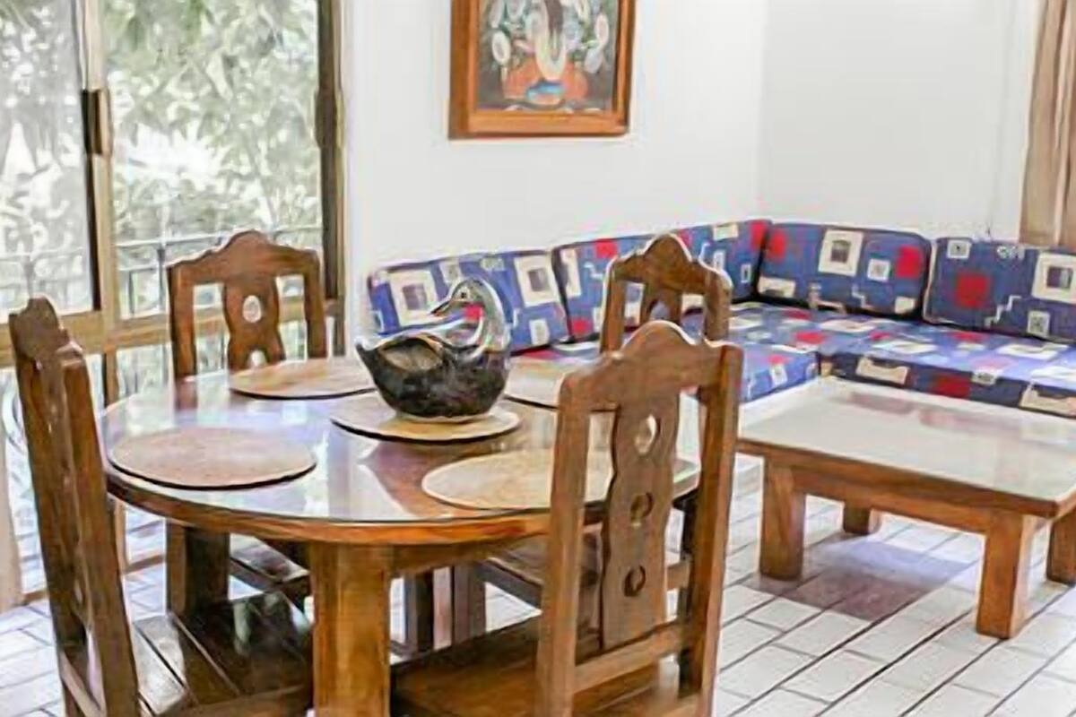 Un coin repas comprenant une table ronde, quatre chaises en bois, un canapé à motifs et une petite table.
