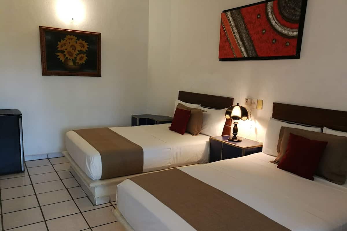 Une chambre d’hôtel avec deux lits, une table de chevet avec une lampe, une petite table et un tableau au mur.