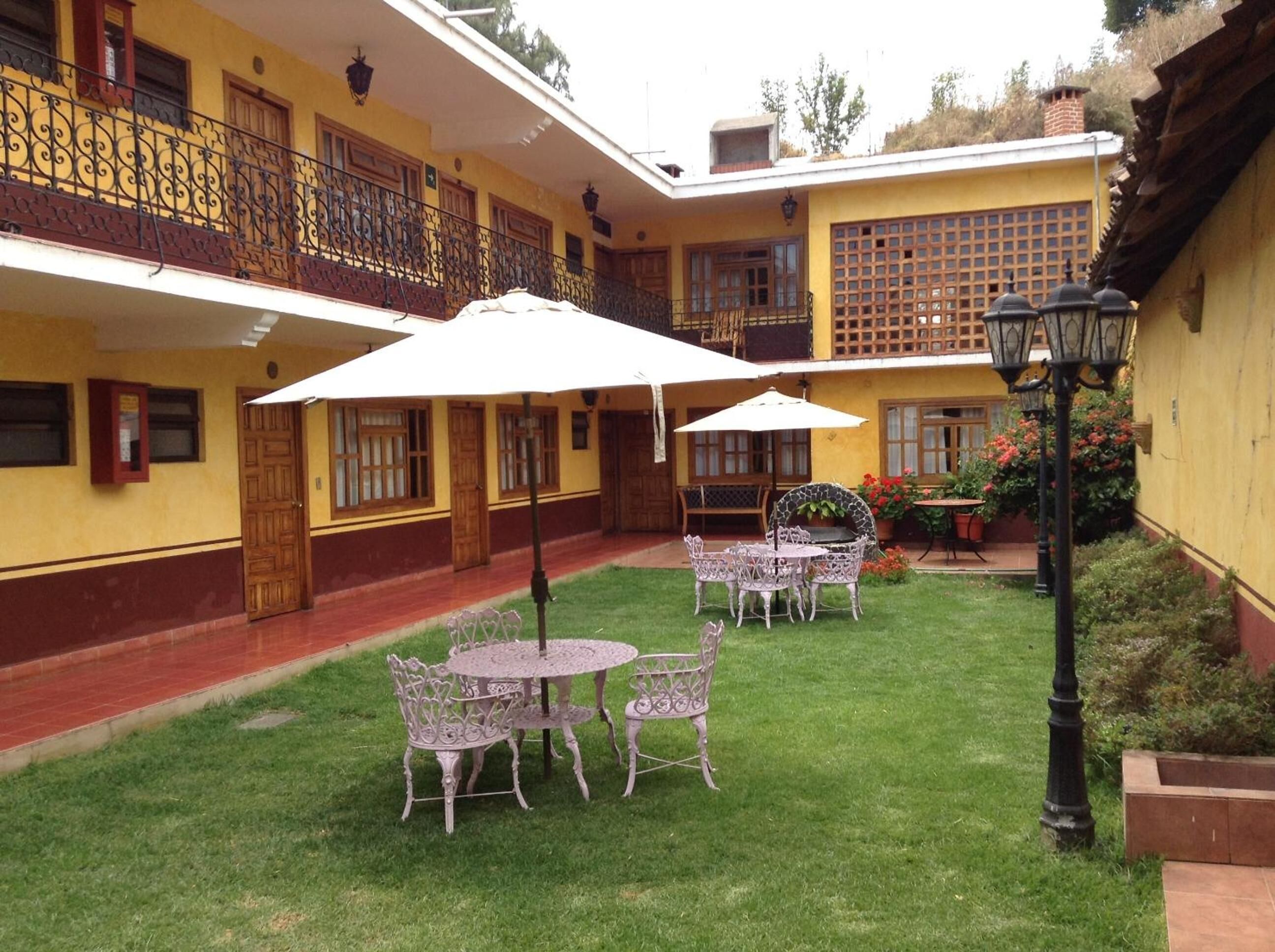 Un patio con zona de comedor, que incluye una mesa y sillas, rodeado por un edificio amarillo con balcones y suelo de tejas rojas.