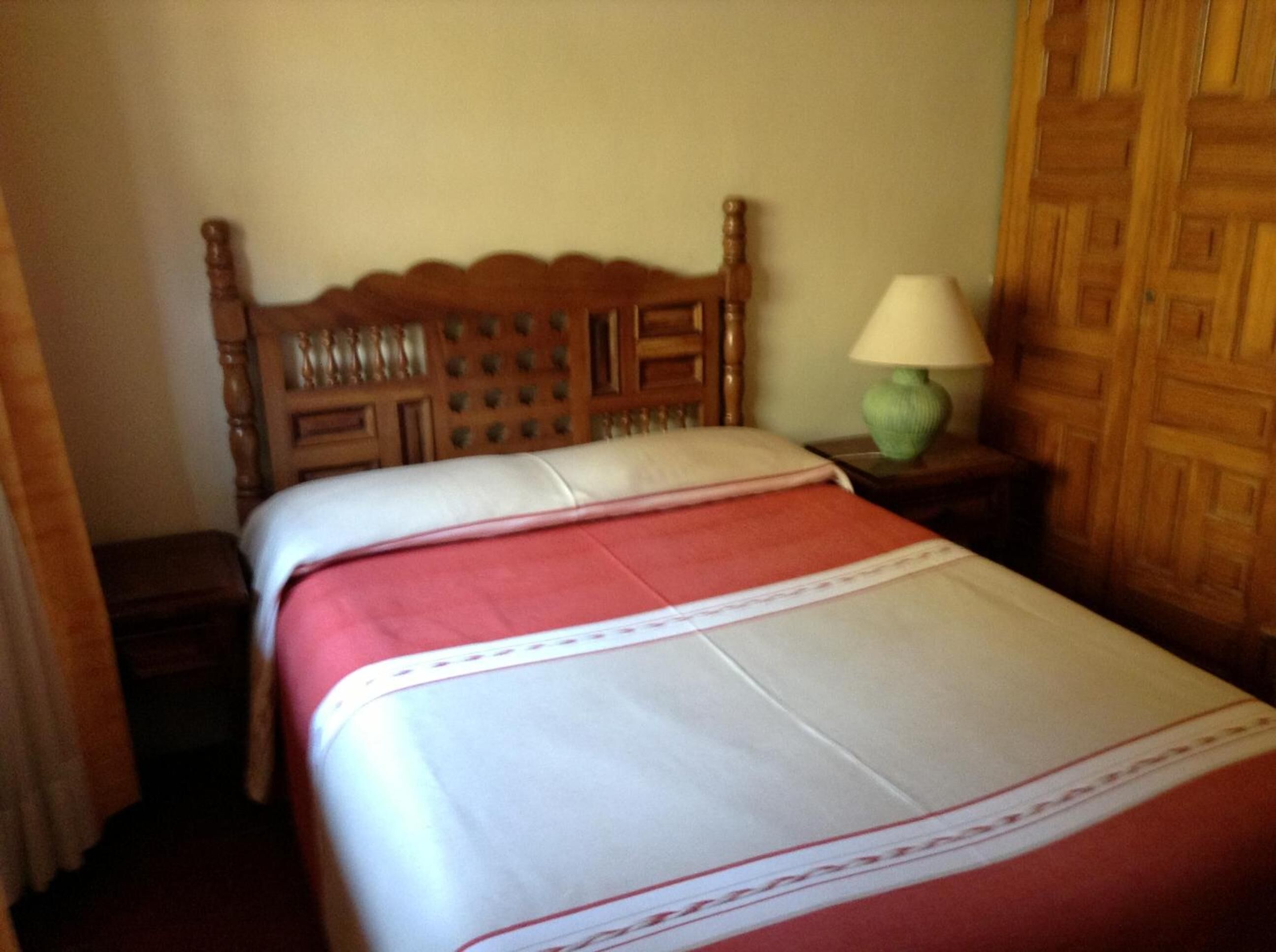 A neatly made bed with a wooden headboard and a green lamp on a bedside table.