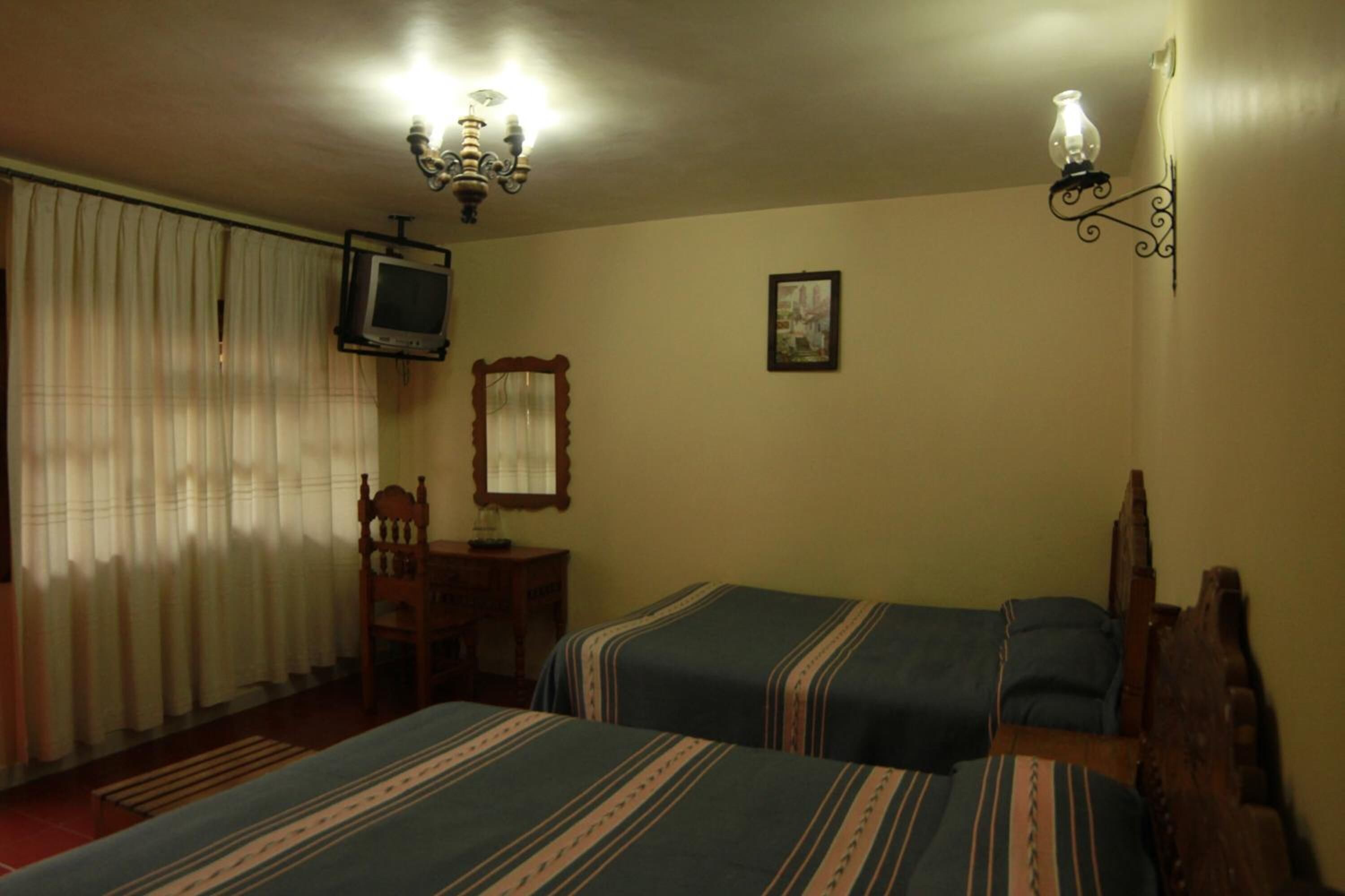 Una habitación con dos camas, televisión, candelabro, espejo y un cuadro en la pared.