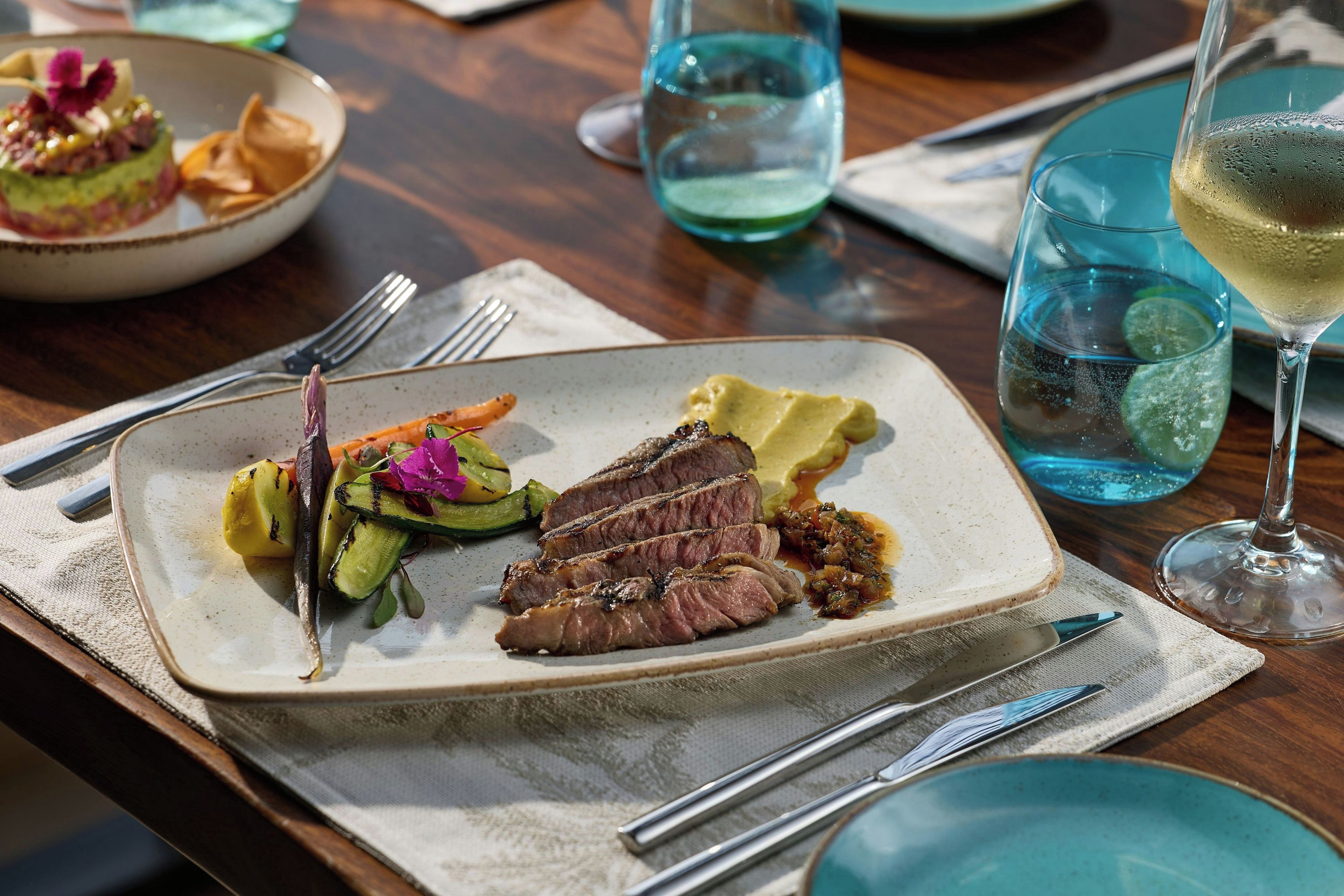A dining table with a plate of food, a glass of wine, and cutlery.