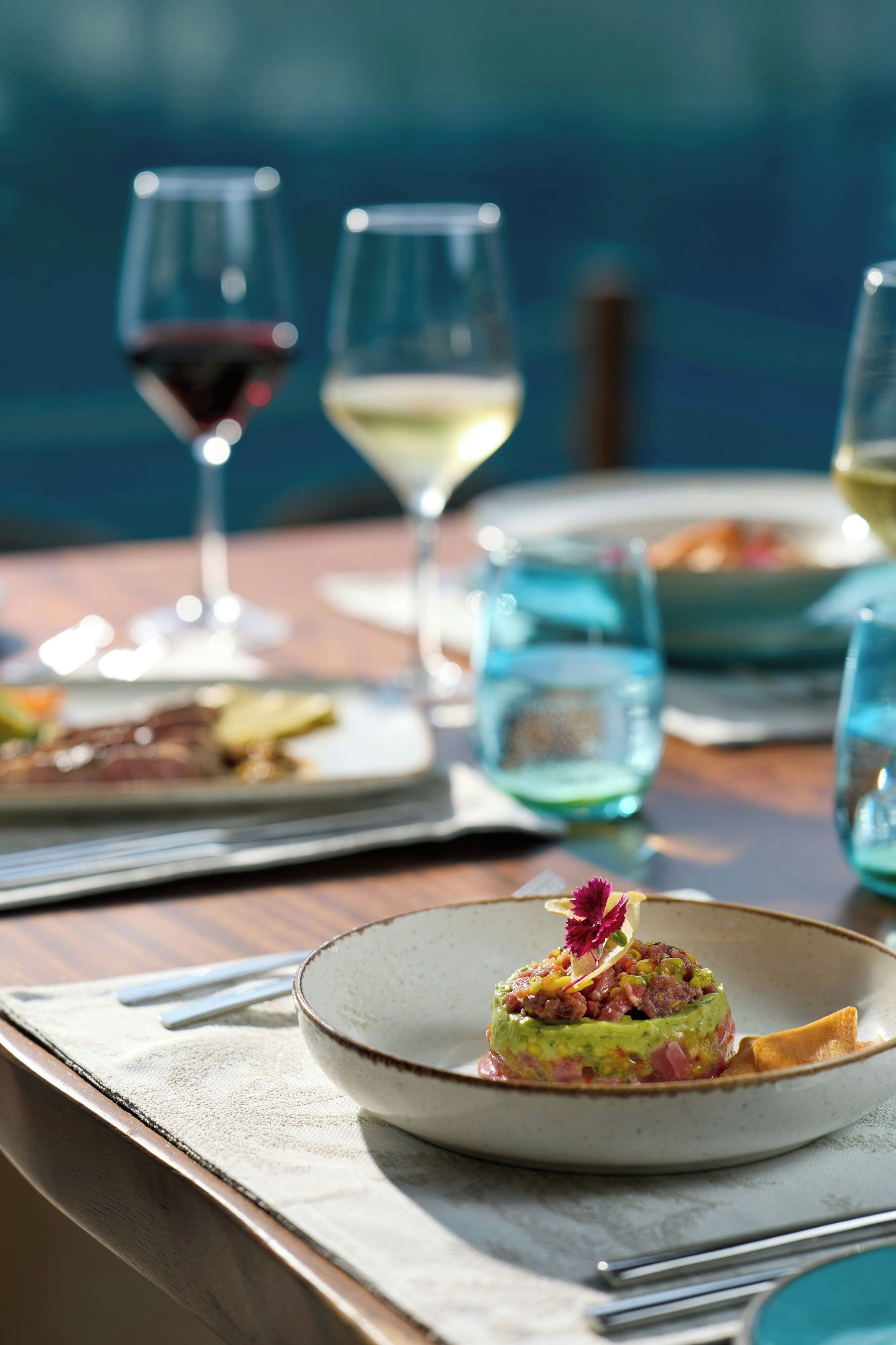 Een eettafel met borden eten, glazen wijn en uitzicht op zee.